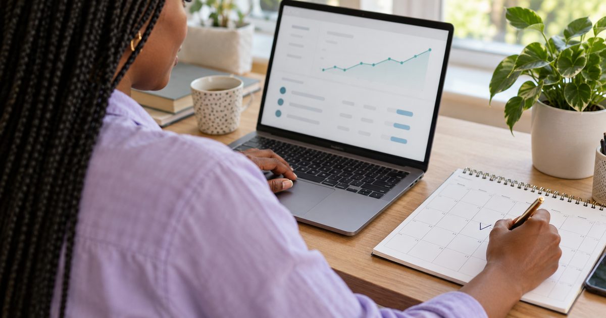 Woman tracking progress on a laptop chart while marking dates on a paper calendar